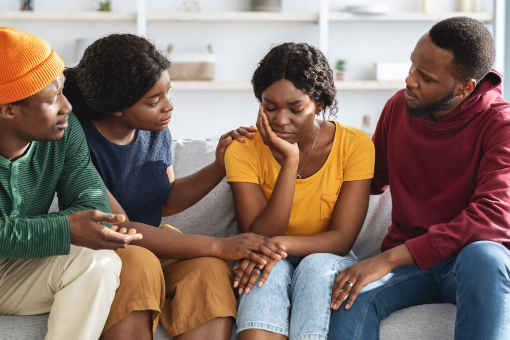 Group of friends comforting a woman on a couch, representing community mental health, emotional support, and compassion.